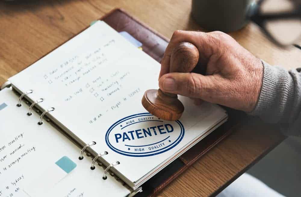 Persona estampando un sello de "Patented" sobre una libreta de planificación, simbolizando la protección legal de una idea o producto. Ideal para ilustrar temas relacionados con el registro de marca en España y la importancia de proteger la propiedad intelectual.